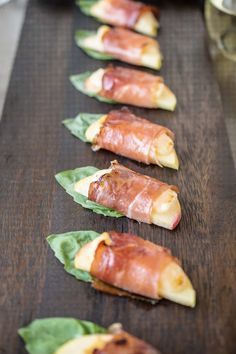 four pieces of bacon wrapped in leafy greens on a wooden table with other food items