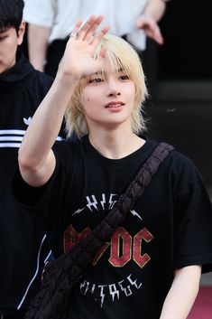 a young man with blonde hair waves to the crowd while wearing a black t - shirt