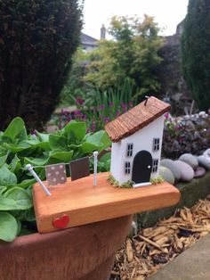 a small white house sitting on top of a wooden planter filled with green plants