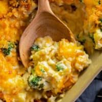 a casserole dish with broccoli and cheese on it, next to a wooden spoon