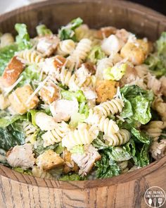 a wooden bowl filled with pasta salad and chicken pieces on top of lettuce