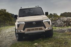 the front end of a beige truck parked on top of a grass covered field next to rocks