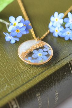 three necklaces with blue flowers on them sitting on top of a green bookshelf