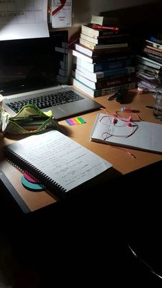 a laptop computer sitting on top of a wooden desk next to a pile of books