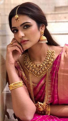 a woman in a pink saree with gold jewelry on her neck and hands near her face