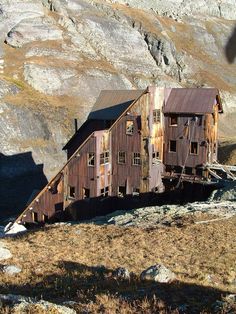 an old wooden building sitting on top of a rocky hill next to a mountain range