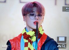 a woman with pink hair and glasses holding a microphone in front of her face while wearing a scarf