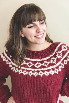 a woman wearing a red and white sweater smiles at the camera with her hands on her hips