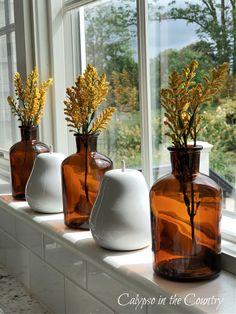 three vases with flowers in them sitting on a window sill