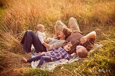 a family laying on a blanket in the middle of a grassy field with tall grass