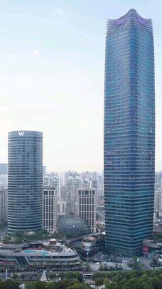 an aerial view of two tall buildings in a city with lots of trees on the other side