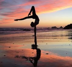 a woman doing a handstand on the beach at sunset with her reflection in the wet sand