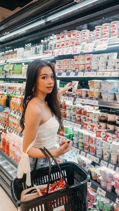 a woman standing in front of a grocery aisle holding a shopping basket and looking at the camera