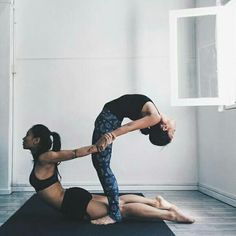 two women doing yoga poses in an empty room with one holding the other's leg