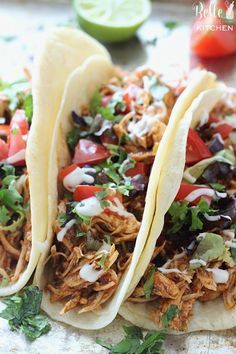 three tacos with shredded meat, tomatoes, black beans and cilantro on top