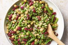 a white bowl filled with green beans and other food items next to a wooden spoon