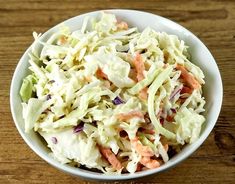 a white bowl filled with coleslaw on top of a wooden table