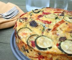 a pizza with zucchini and tomatoes on it next to a fork, knife and napkin