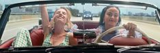 two women sitting in a convertible car on the road