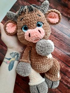 a hand holding a small stuffed animal in it's left arm, on top of a wooden table