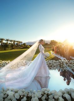 the bride is walking down the aisle with her veil blowing in the wind and flowers all around her