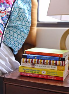 a stack of books sitting on top of a wooden table next to a lamp and pillow