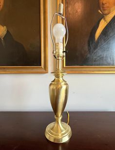 an old fashioned lamp is sitting on a table in front of two paintings with portraits