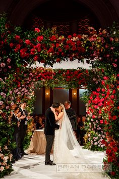 the bride and groom are getting married in front of an archway with flowers on it