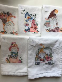 four white towels with embroidered pictures of pumpkins, gnomes and cars on them