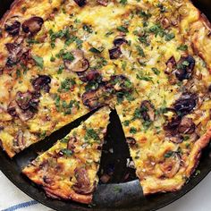 a pizza with mushrooms, cheese and herbs cut into slices on a black plate next to a white towel