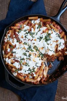 a skillet filled with pasta and cheese on top of a blue cloth next to a wooden table