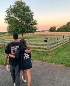 a man and woman walking down a road towards a fenced in area with horses