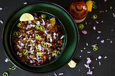 a green bowl filled with beans and onions next to a jar of mustard, lemon wedges and confetti