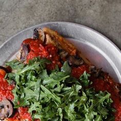 a pizza with mushrooms and greens on it in a metal plate sitting on a table