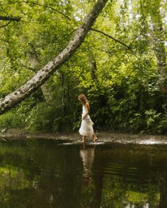 a woman walking across a river in the woods