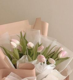 a bouquet of tulips wrapped in white paper and tied with pink ribbon on a table