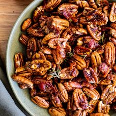 a bowl filled with pecans on top of a wooden table next to a knife and fork