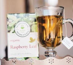 a glass cup filled with tea next to a box of organic raspberry leaf