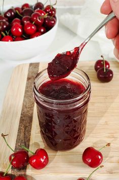 someone is spooning cherries into a jar of cherry jam on a cutting board