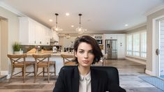 a woman sitting at a table in front of a kitchen and dining room with an open floor plan