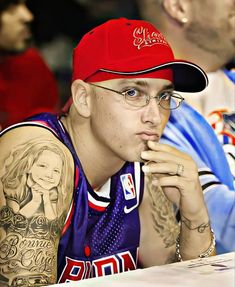 a man with tattoos on his arms and shoulder sitting at a table in front of other people