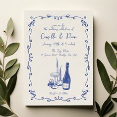 a blue and white wedding save the date card with greenery around it on a table