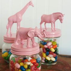 three jars filled with candy and giraffes on top of a wooden table