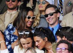 a group of people sitting next to each other at a tennis match, all wearing sun glasses