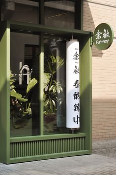 a green store front with chinese writing on the window and large white tube in it