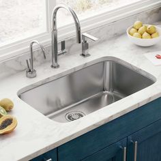 a kitchen sink with two faucets and bowls of fruit on the counter top