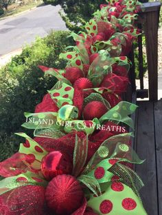 red and green christmas wreaths on the side of a wooden deck with trees in the background