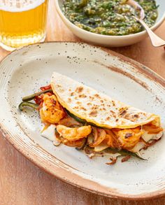 a white plate topped with food next to a bowl of soup and a glass of beer