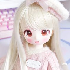 a doll with long blonde hair wearing a pink sweater and bow, sitting in front of a computer keyboard