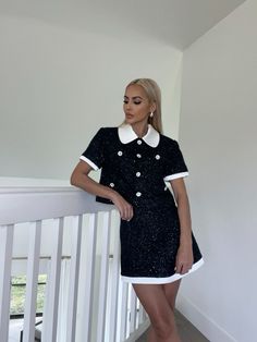 a woman in a short black dress and white collared shirt standing on a balcony